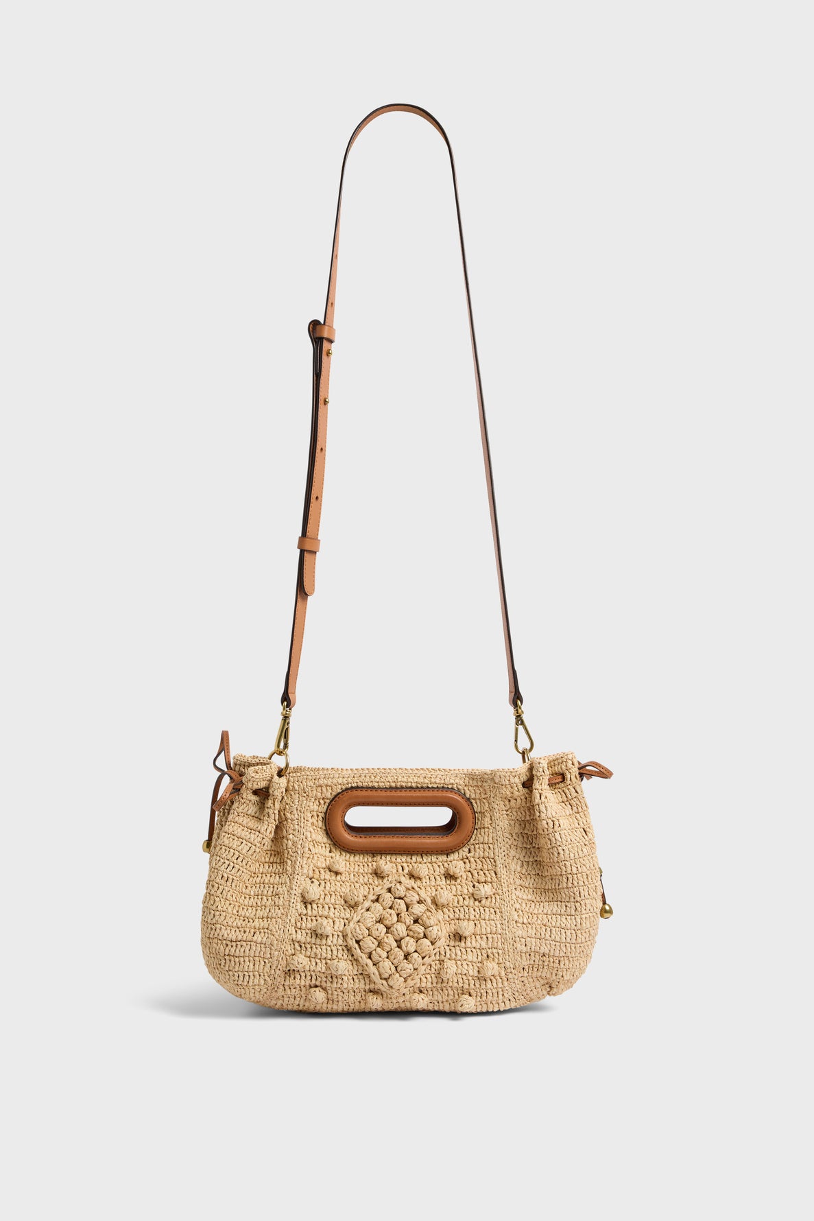 A woven beige crossbody sac à main crafted from raphia naturel, featuring a brown adjustable leather strap and an oval-shaped wooden handle, with a beautifully textured pattern on the front for an artisanal touch.