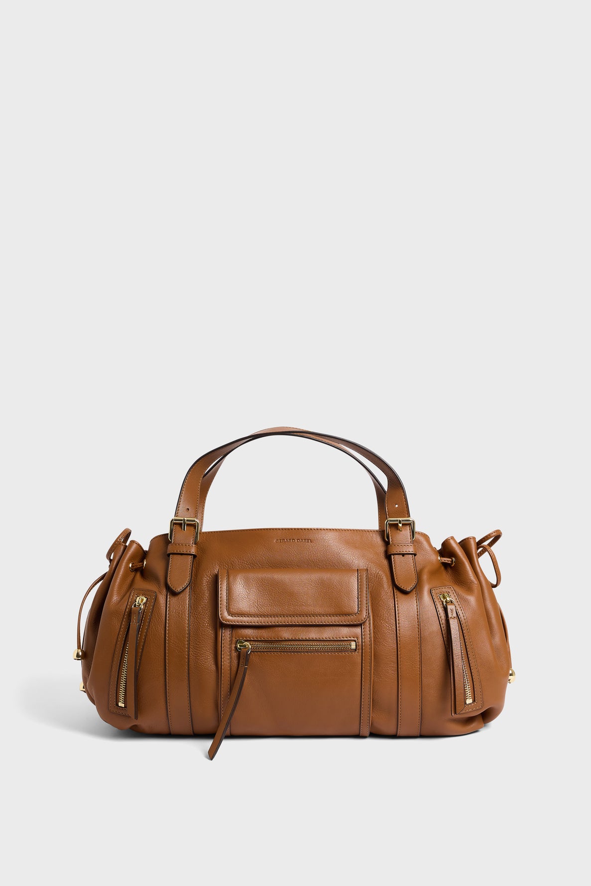 A brown sac à main in cuir délicat with dual handles, front zipper pocket, gold zippers, and side poches zippées on the sides, shown against a plain white background.