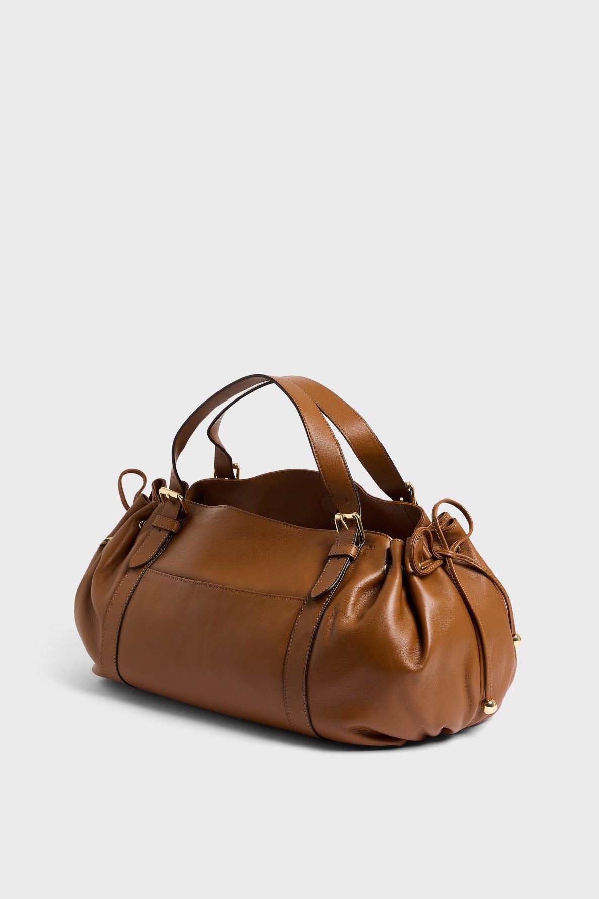 A brown leather sac à main with short handles, gold hardware, and gathered sides, crafted from cuir délicat and shown on a plain light background.