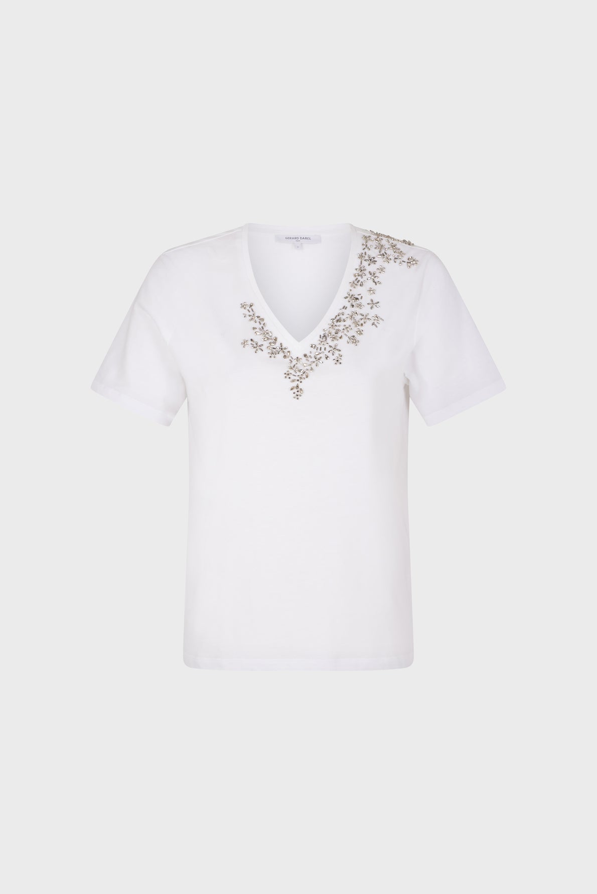White short-sleeve T-shirt col V in soft coton, featuring small, delicate floral embroidery in light brown and gold colors arranged along the neckline and extending slightly onto the left shoulder. Subtle strass accents add a hint of sparkle to the elegant design. The shirt is displayed against a plain background.