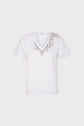 White short-sleeve T-shirt col V in soft coton, featuring small, delicate floral embroidery in light brown and gold colors arranged along the neckline and extending slightly onto the left shoulder. Subtle strass accents add a hint of sparkle to the elegant design. The shirt is displayed against a plain background.