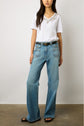 A person wearing a white short-sleeve T-shirt col V en coton with floral embroidery, light blue wide-leg jeans, a black belt, and black sandals stands against a plain background. Subtle strass details add a touch of sparkle to the look.