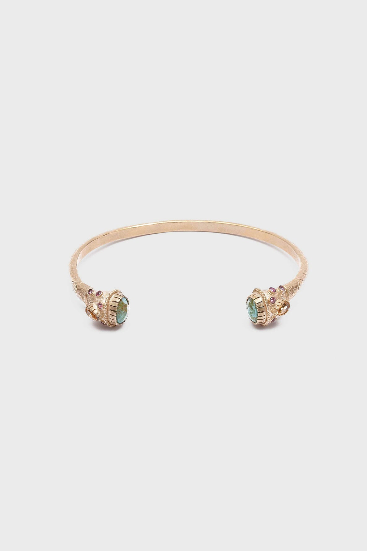 Gold open cuff bracelet laiton featuring ornate ends set with green gemstones reminiscent of pierre turquoise and small decorative accents on a white background.