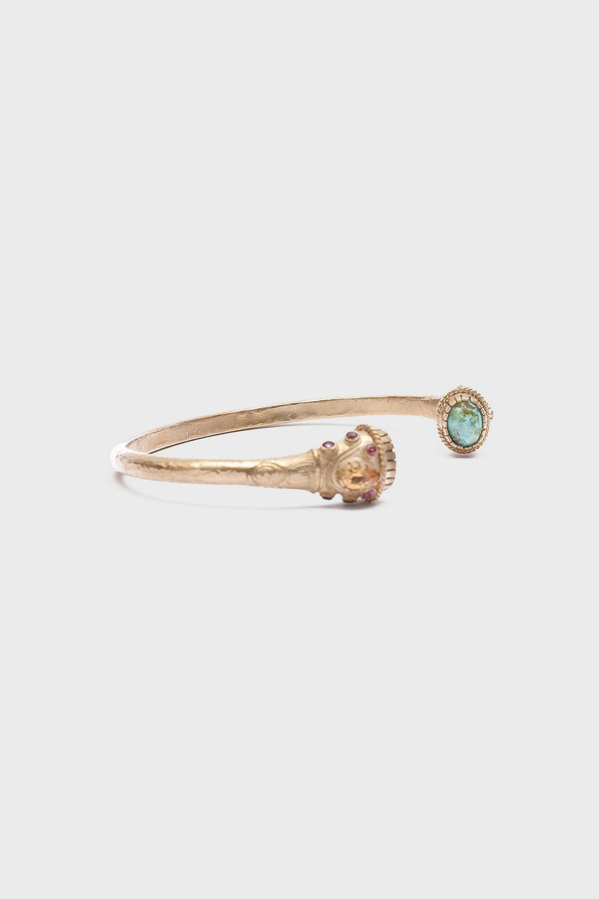 A gold open cuff bracelet laiton with a striking lion head detail on one end and a round pierre turquoise stone set in a gold bezel on the other end, shown on a plain white background.