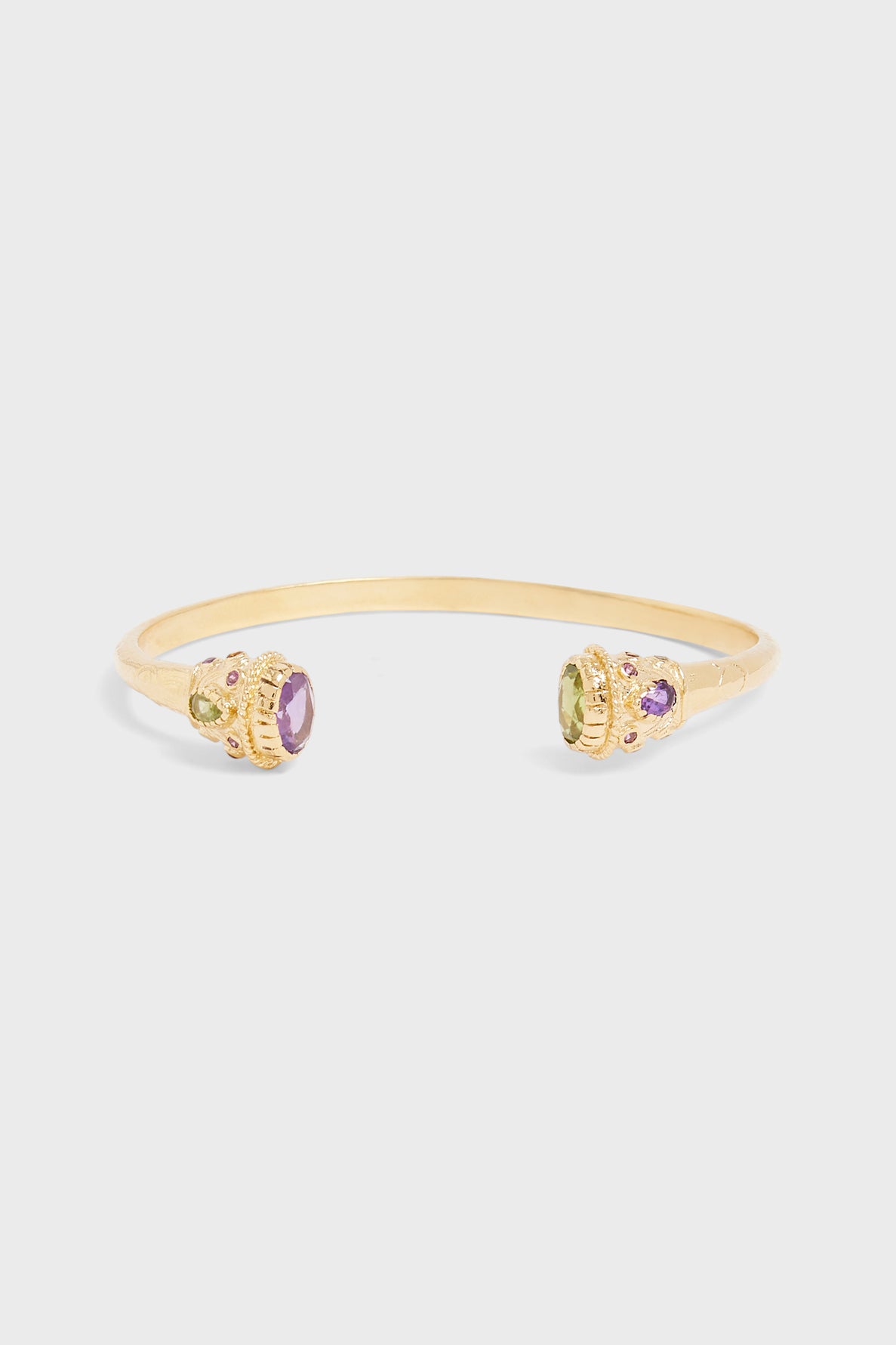 A gold open cuff bracelet plaqué or with round purple and green gemstones set in decorative settings on each end, including a striking pierre labradorite, displayed on a plain white background.