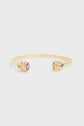 A gold open cuff bracelet plaqué or with round purple and green gemstones set in decorative settings on each end, including a striking pierre labradorite, displayed on a plain white background.